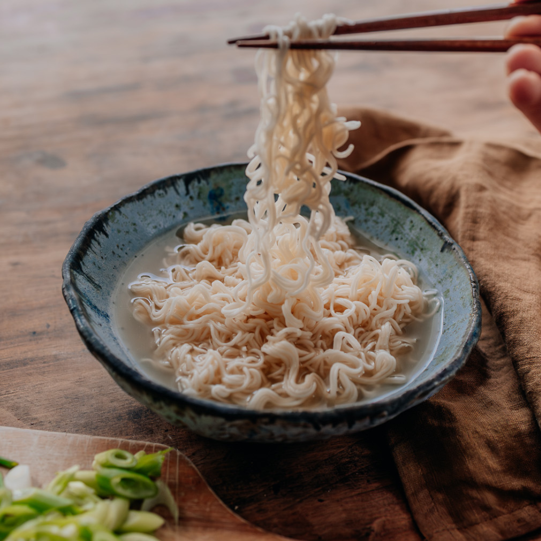 Noodles being lifted with chopsticks from a bowl on a wooden table